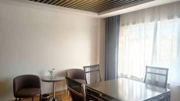 Una habitación de hotel moderna con una mesa de comedor, dos sillas, una mesita auxiliar y un ventanal con cortinas.