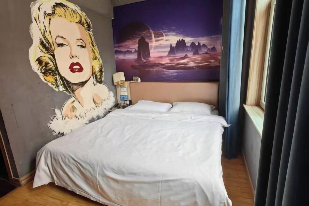 Een slaapkamer met een bed, een muurschildering, een nachtkastje en een raam met gordijnen.
