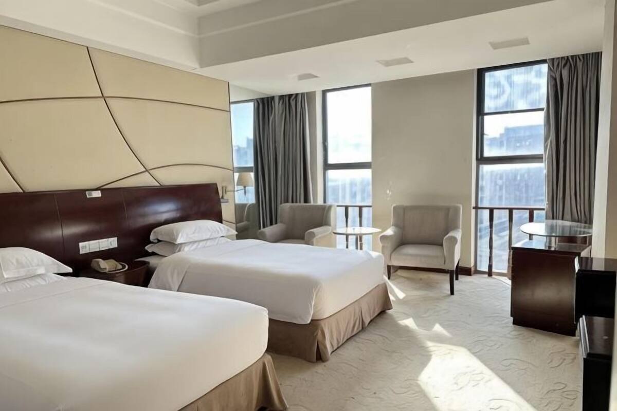 Een hotelkamer met twee bedden, een bank, een stoel, een kleintje tafeltje en grote ramen.