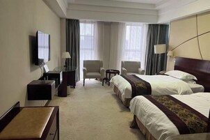 Habitación de hotel con dos camas, un escritorio, una silla, un televisor y una lámpara.