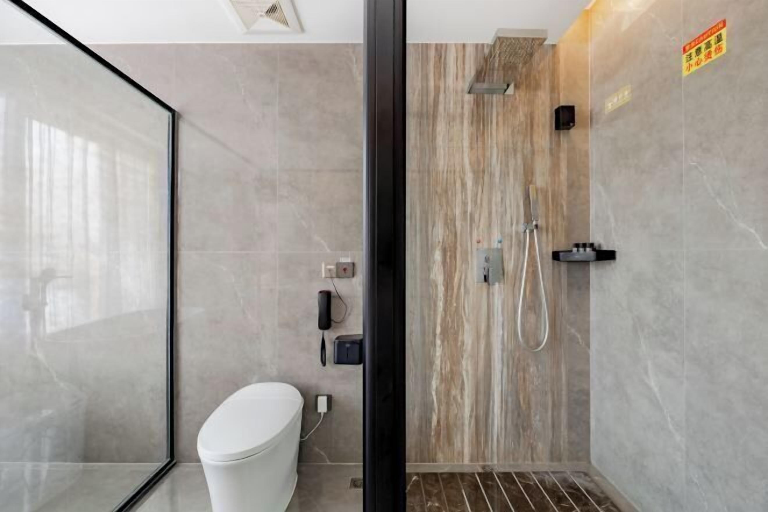 A modern bathroom with a glass shower enclosure, a toilet, and a marble wall.