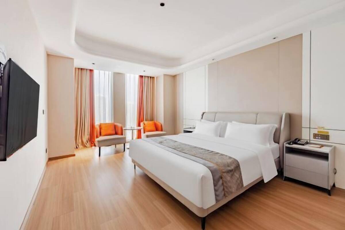 Een moderne hotelkamer met een groot bed, een nachtkastje met een lamp, een stoel en een aan de muur bevestigde televisie.