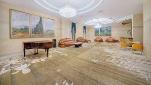 Une pièce spacieuse avec un grand piano, des canapés en cuir, un lustre et un grand tableau accroché au mur.