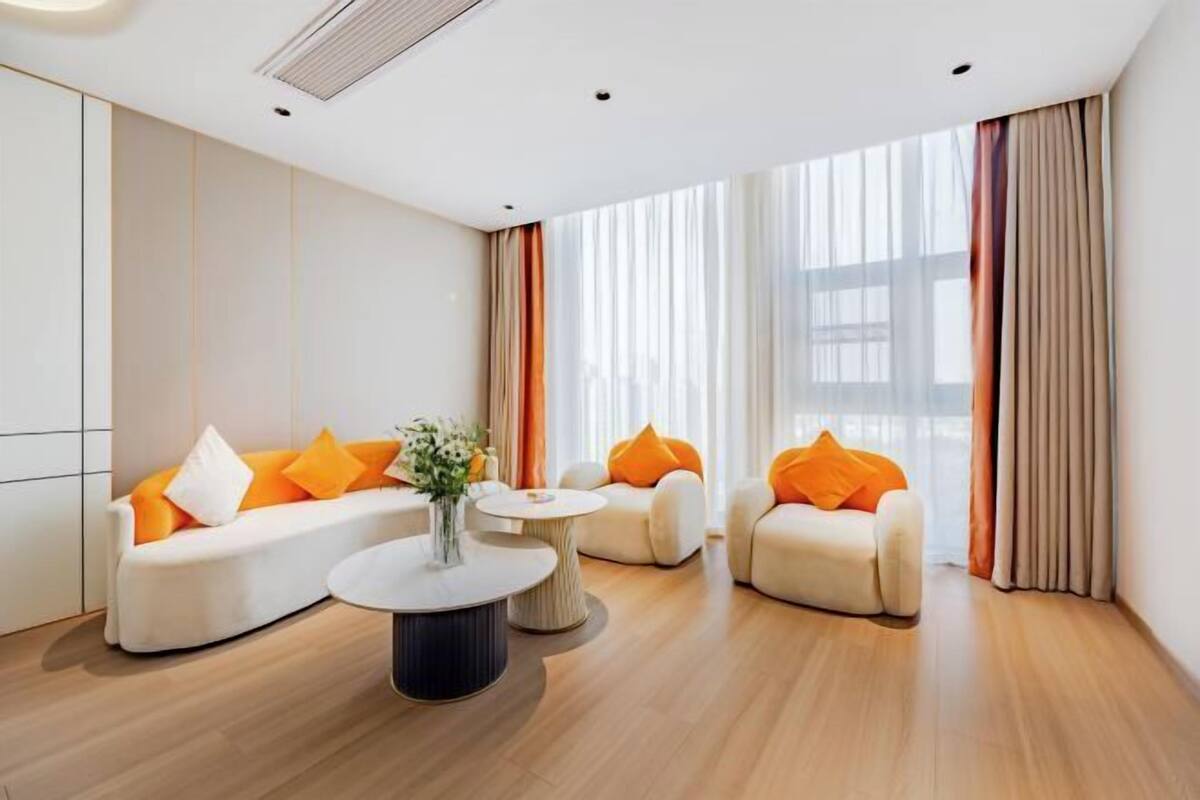 Een moderne hotelkamer met een bank, fauteuils, een ronde salontafel en grote ramen met gordijnen.