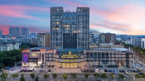 Un hôtel moderne doté d’une entrée imposante, d’un parking et offrant une vue sur le paysage urbain en arrière-plan.