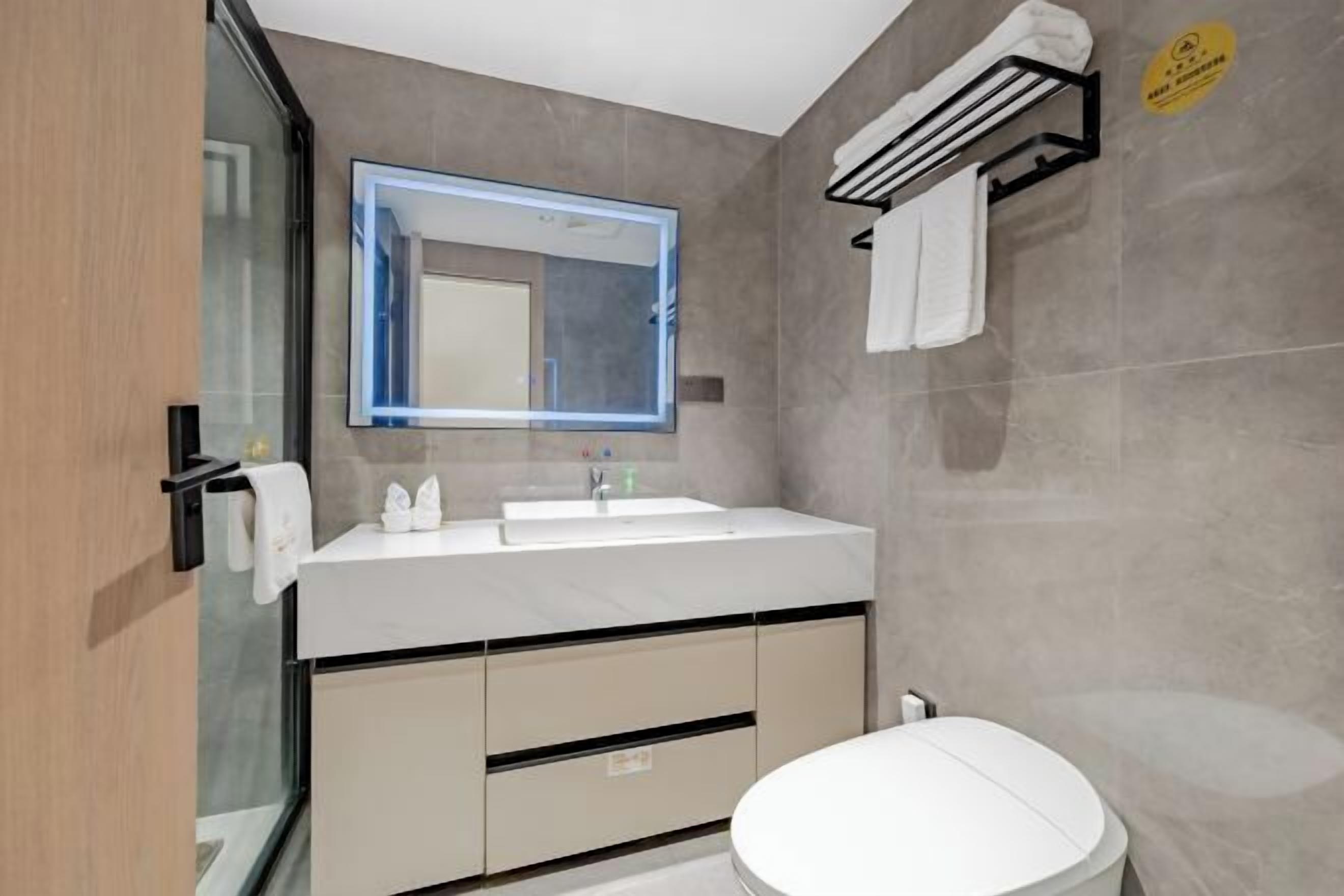 A modern bathroom with a large mirror, a white sink, and a toilet.