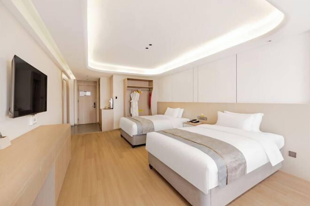 Een hotelkamer met twee bedden, een aan de muur bevestigde televisie, een kledingkast en een spiegel.