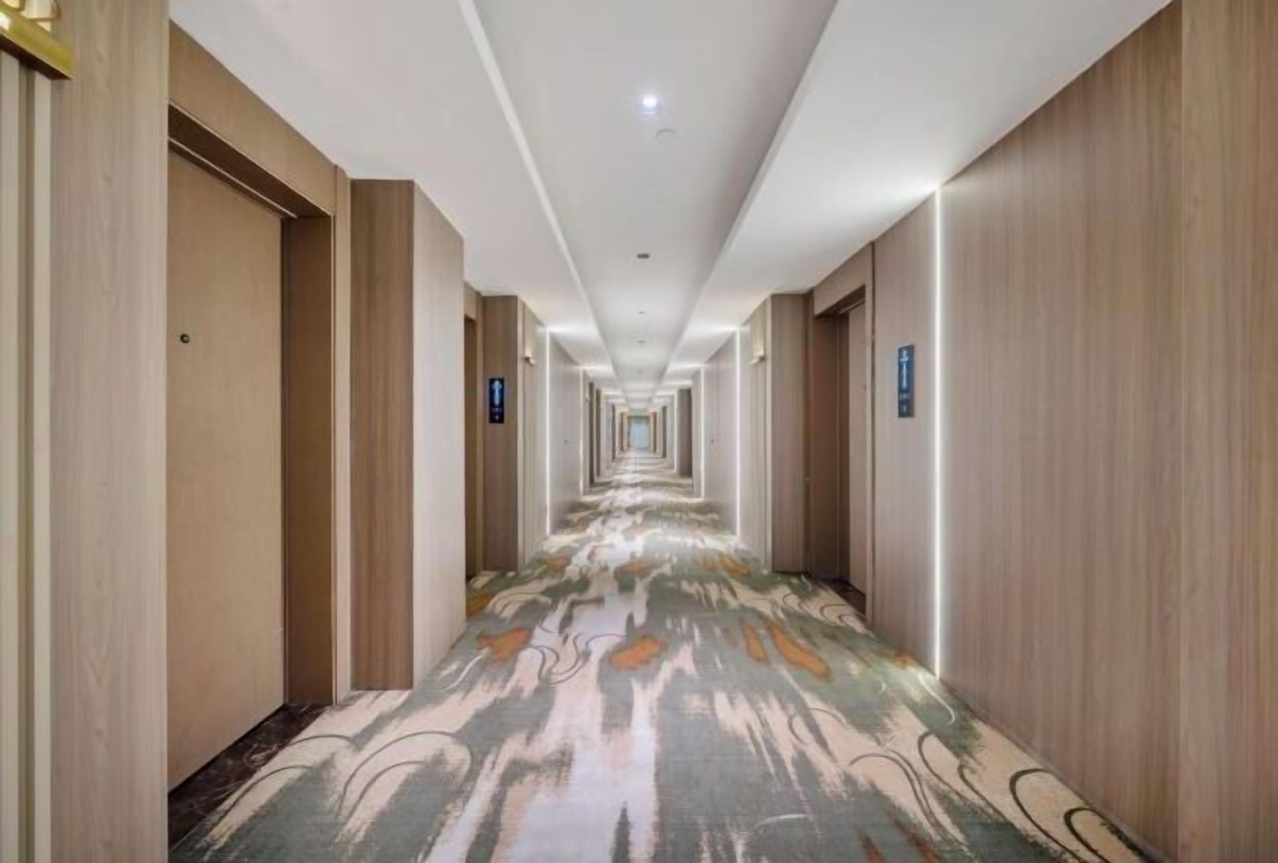 Un largo y estrecho pasillo de hotel con paneles de madera en las paredes y una alfombra estampada.
