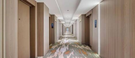 Un largo y estrecho pasillo de hotel con paneles de madera en las paredes y una alfombra estampada.
