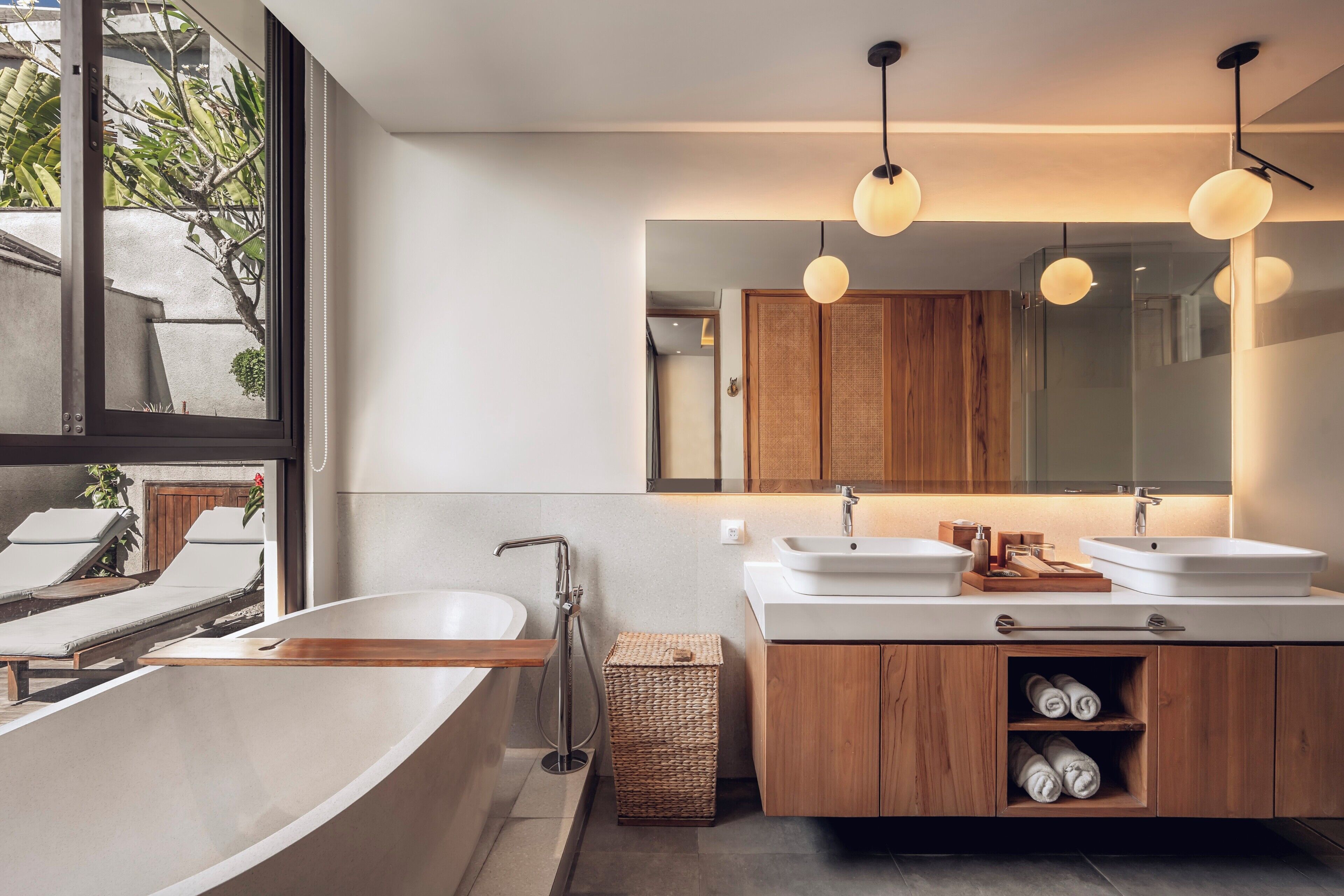 Un bagno moderno con una vasca freestanding, due lavabi, mobili in legno e uno specchio grande.