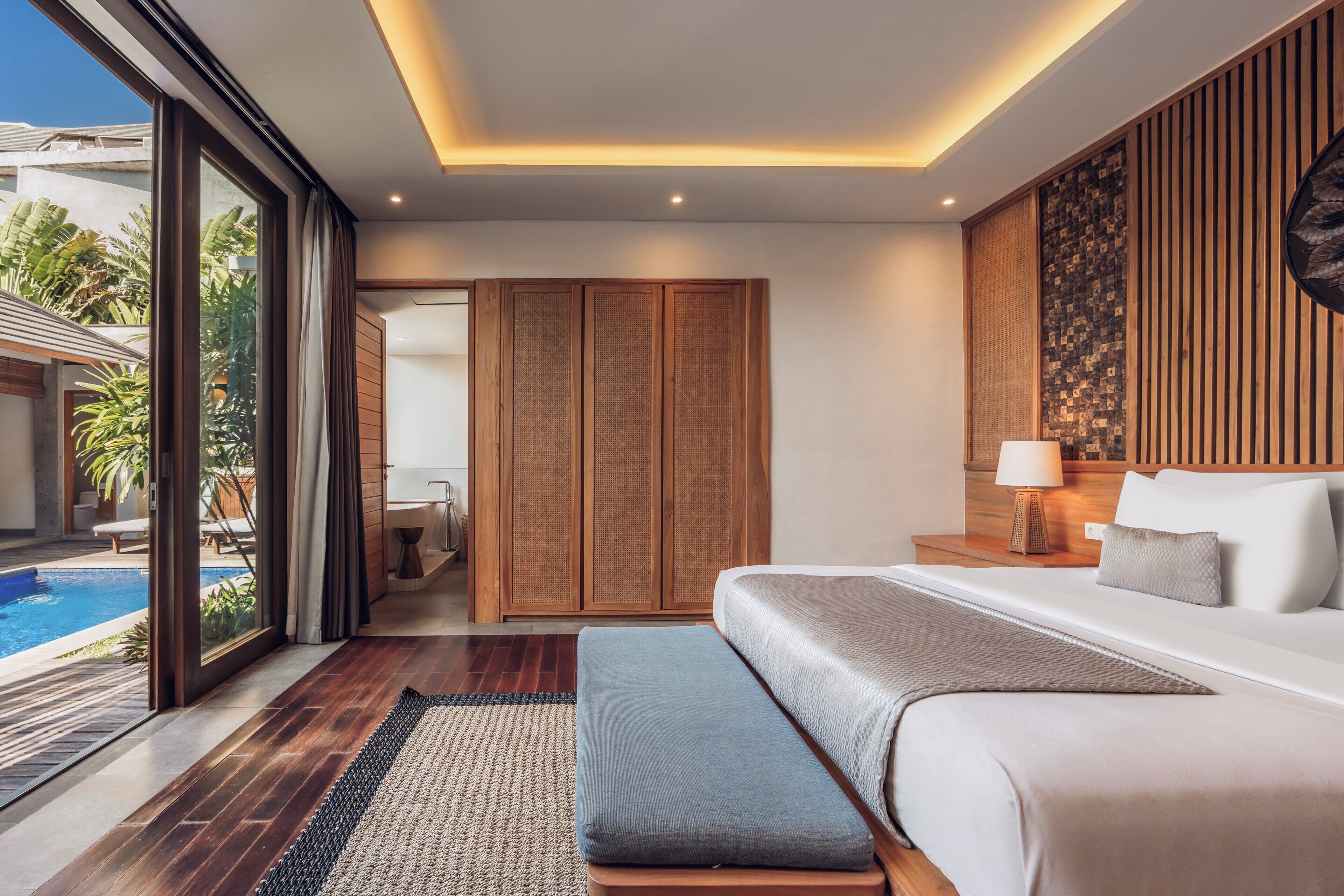 Un dormitorio moderno con una cama grande, una mesita de noche, una lámpara y vistas a una piscina.