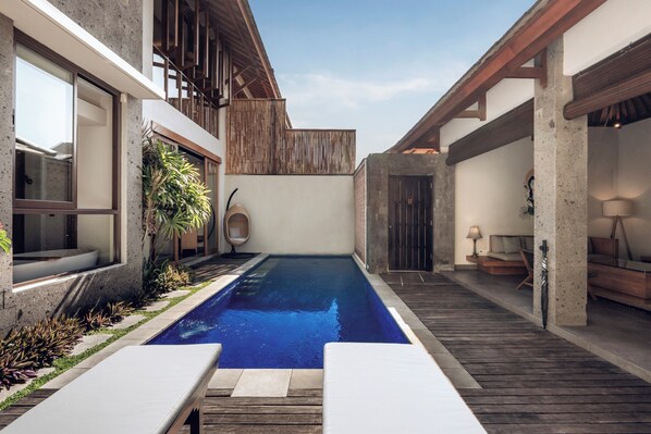 Uma área de piscina moderna com deck de madeira, espreguiçadeiras e uma parede de concreto.