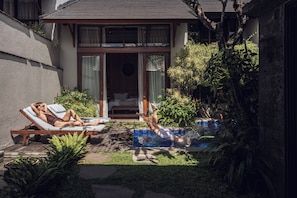 A private pool area with two lounge chairs, a small garden, and a building with a sliding glass door. - Teratai Villa Canggu by Ini Vie Hospitality (Canggu)