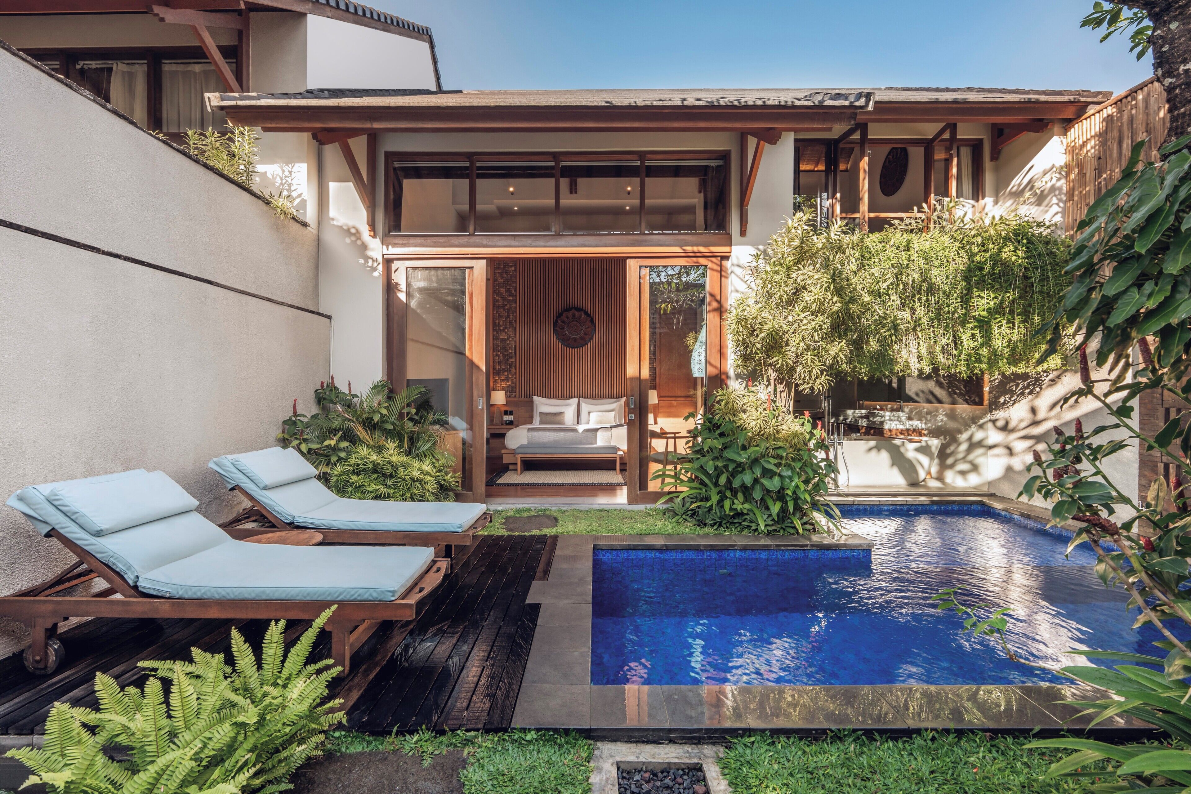 Une maison moderne dotée d’une piscine, de chaises longues et d’un petit jardin.