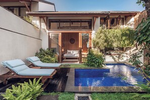 Uma casa moderna com piscina, cadeiras de descanso e um pequeno jardim.