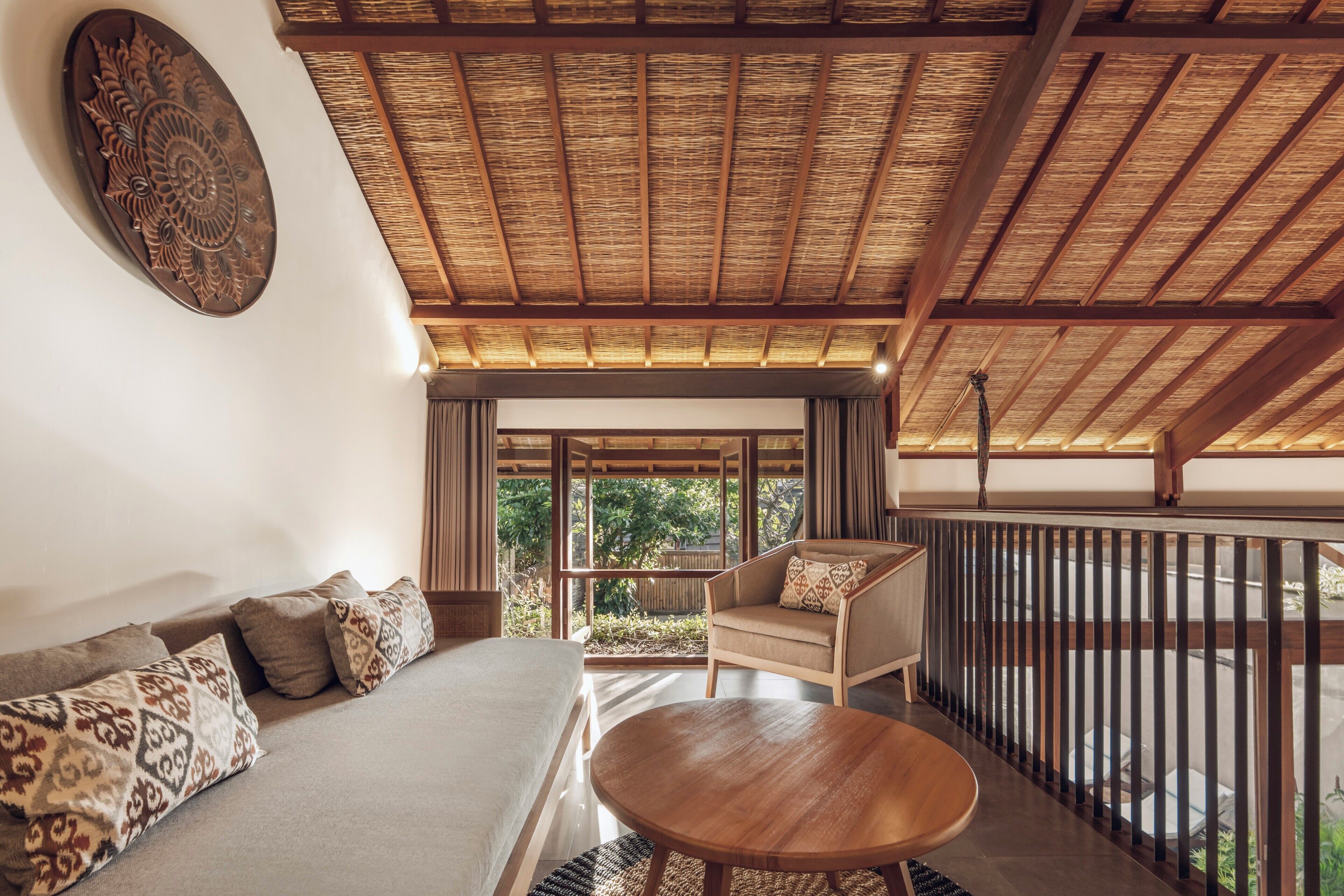 Una habitación con techo de paja, un sofá con cojines estampados, una mesa de madera y vistas al exterior con vegetación.
