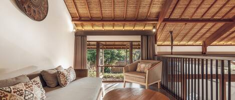 Una habitación con techo de paja, un sofá con cojines estampados, una mesa de madera y vistas al exterior con vegetación.