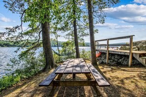Une table de pique-nique en bois, avec des bancs, entourée d’arbres et donnant sur un lac.