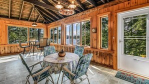 A wooden cabin with a dining area featuring a round table and chairs, large windows, and a wooden ceiling. - Webster Lake Retreat for Nature and Water Lovers (Franklin)