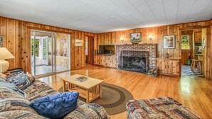 A cozy living room with a fireplace, wooden walls, a sofa, and a television. - Webster Lake Retreat for Nature and Water Lovers (Franklin)