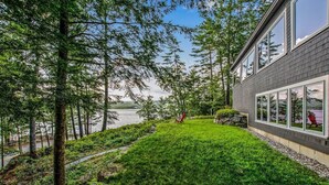 A modern house with a well-maintained lawn, a red chair, and a stone wall. - Webster Lake Retreat for Nature and Water Lovers (Franklin)