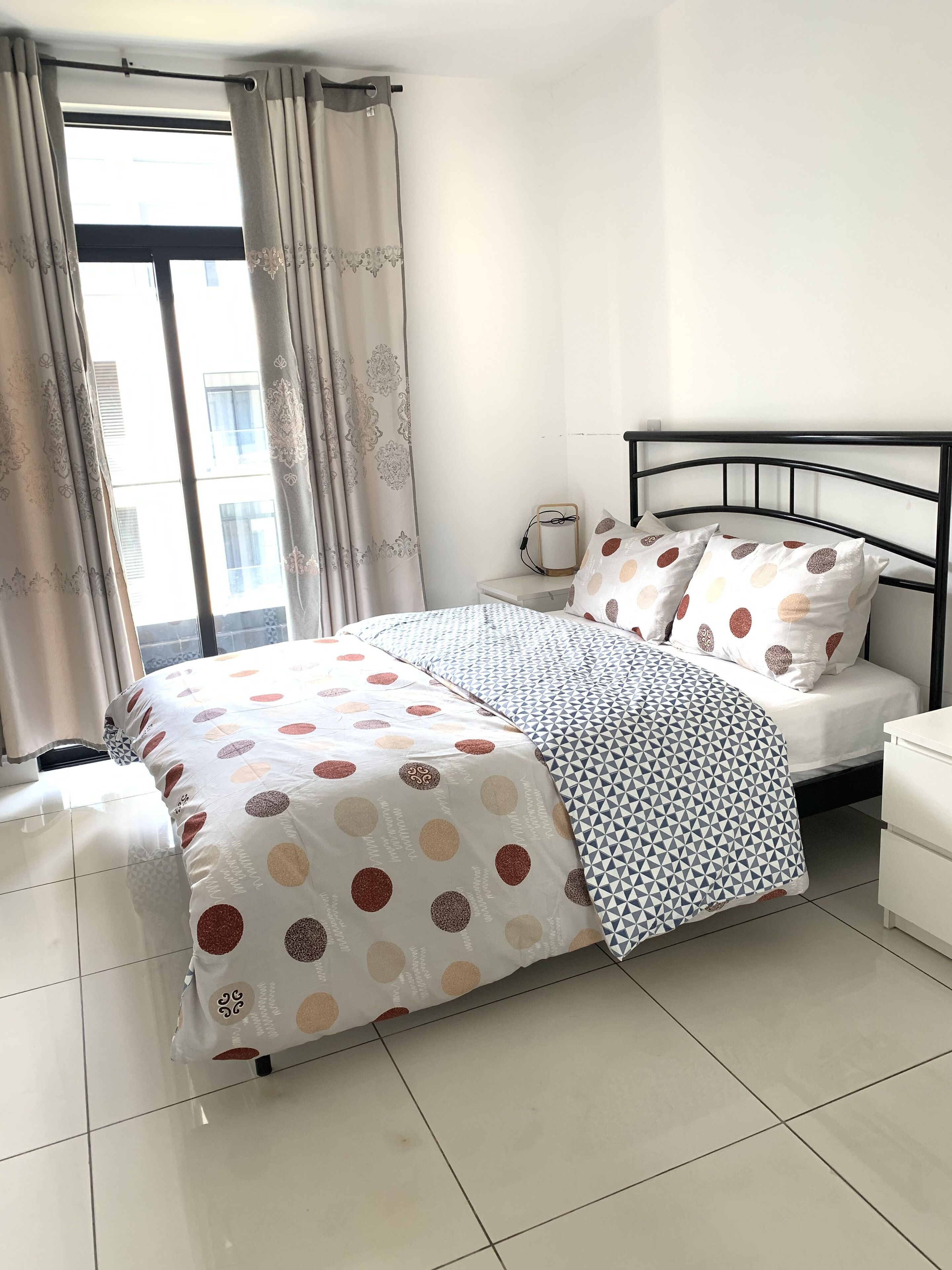 Une chambre à coucher avec un lit, des oreillers, une table de chevet et une fenêtre avec des rideaux.