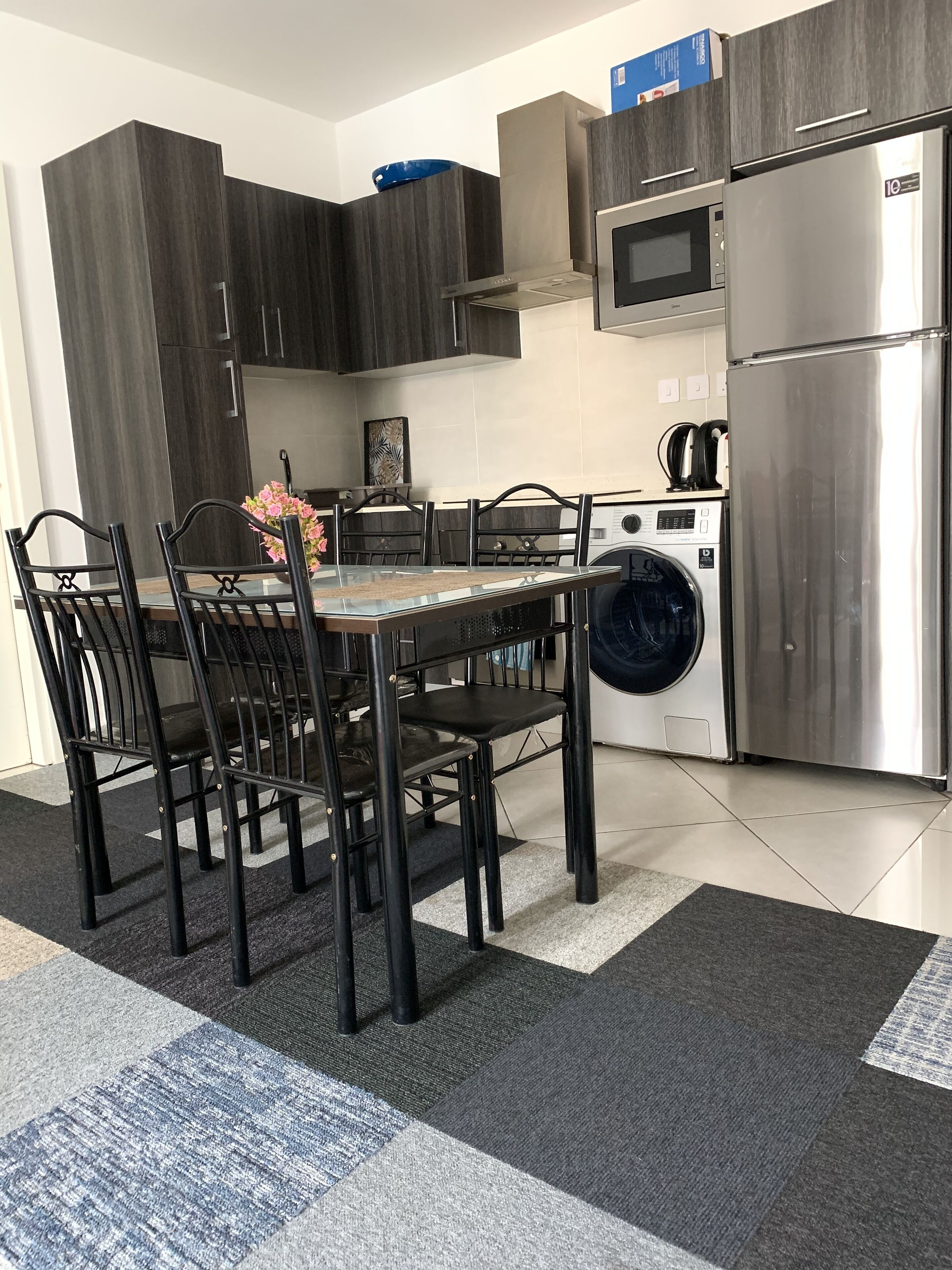 Una cocina moderna con armarios de madera oscura, un refrigerador de acero inoxidable, un microondas y una lavadora.