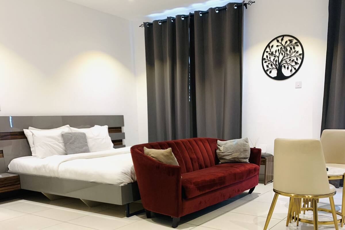 A modern living room with a sofa, a dining table with chairs, and a bed.