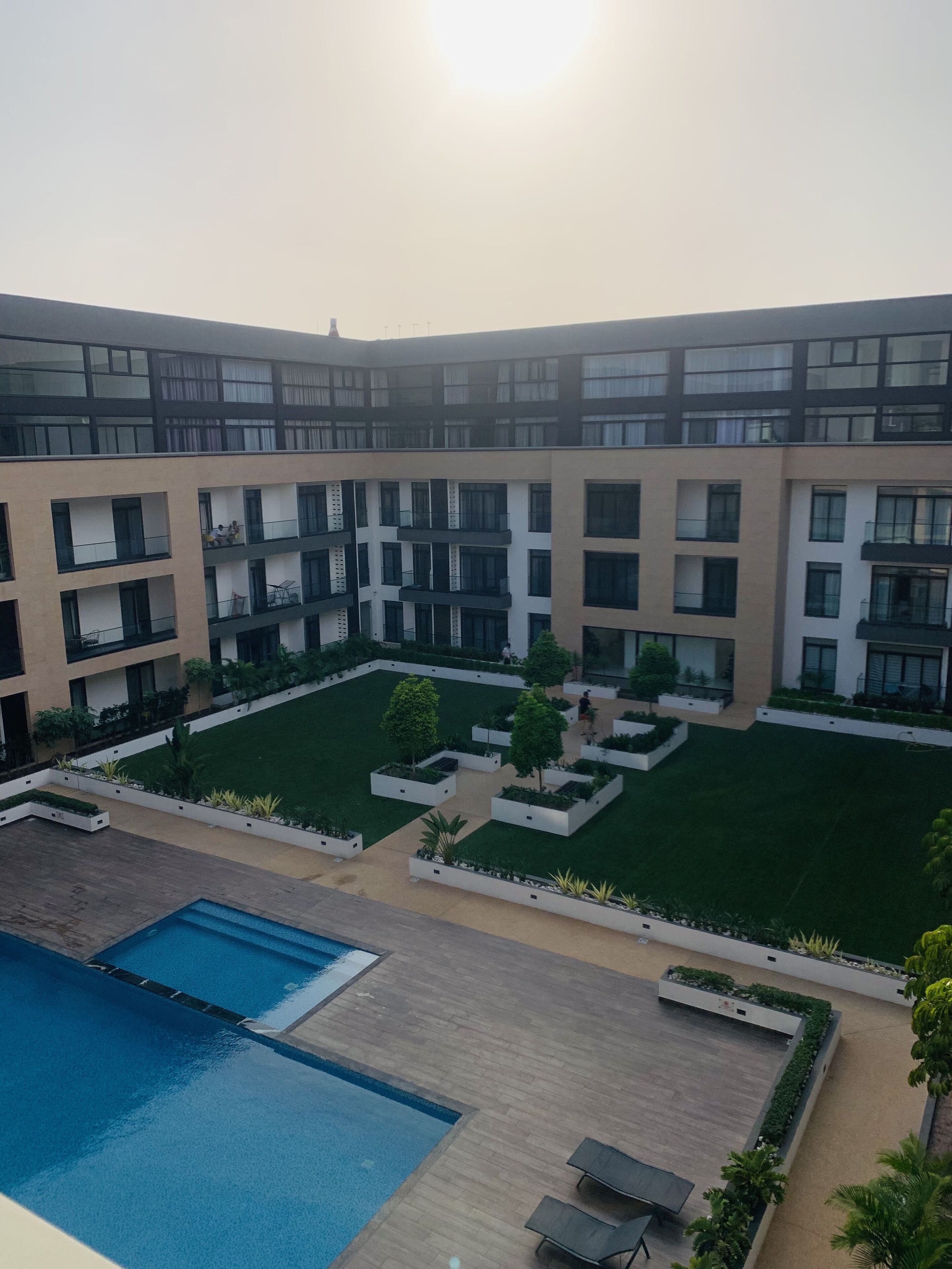 Un bâtiment moderne doté de nombreux balcons, d’une cour intérieure agrémentée de verdure et d’un espace piscine.