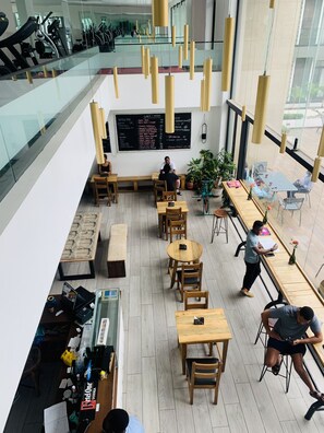 Un café moderno con mobiliario de madera, una pizarra con el menú y vista a un gimnasio al fondo.