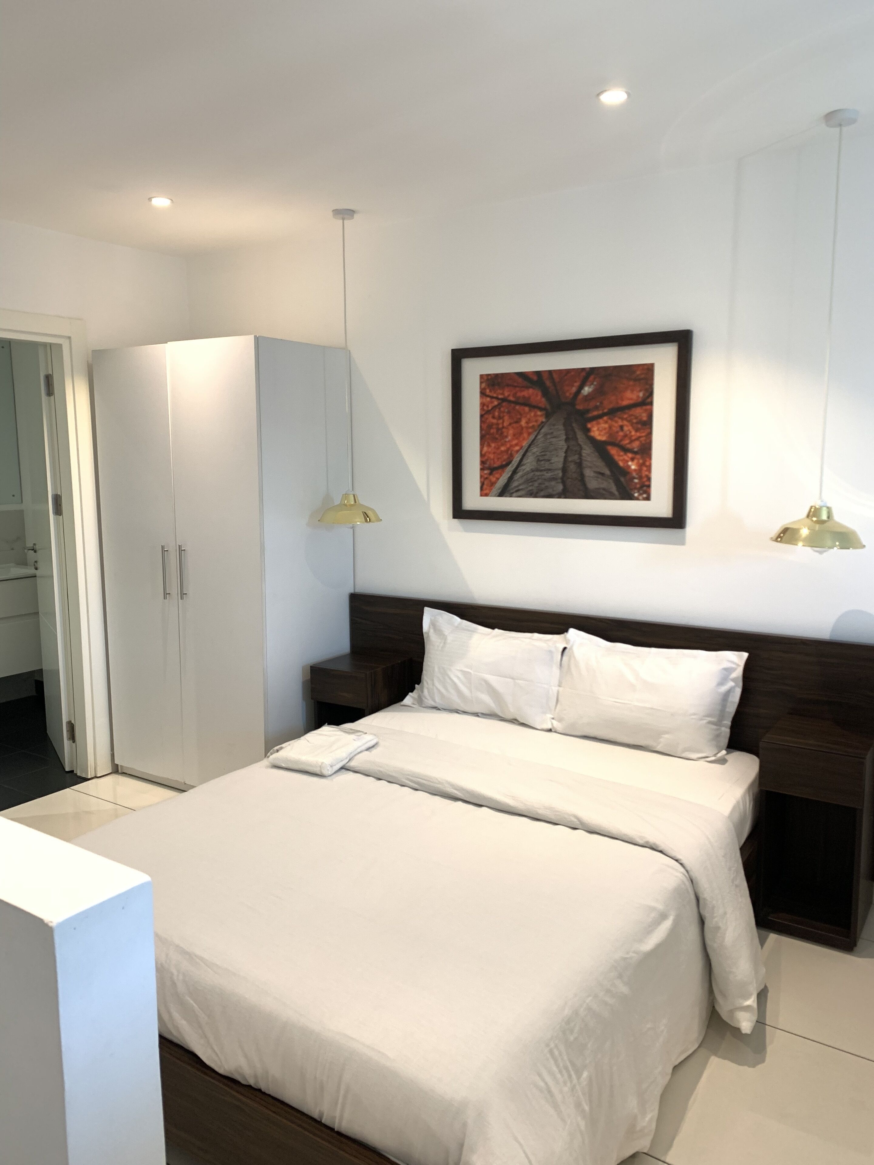 A modern bedroom with a bed, a wardrobe, a nightstand, and a framed picture on the wall.