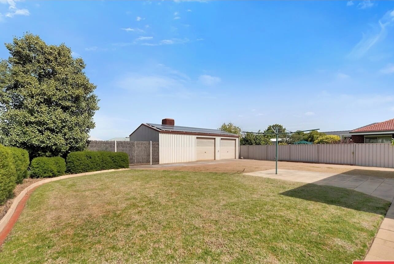 A residential property with a fenced yard, a garage, and a large tree.