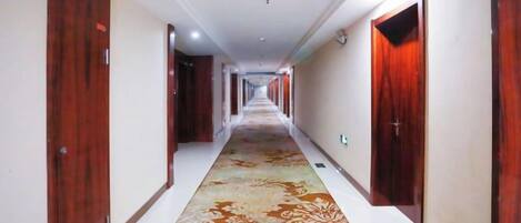 Un pasillo de hotel con puertas de madera, una alfombra estampada y un largo recorrido.