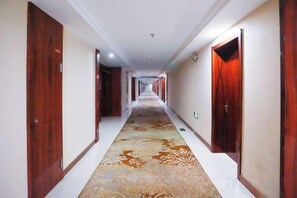 A hotel corridor with wooden doors, a patterned carpet, and a long hallway.