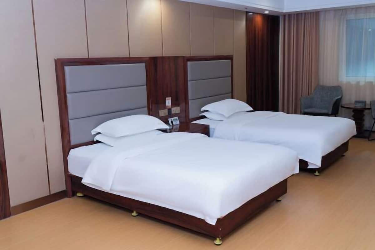 Une chambre d’hôtel avec deux lits, une petite table, une chaise et une fenêtre avec des rideaux.