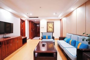 A modern living room with a flat-screen TV, wooden entertainment unit, a sofa with blue cushions, and a coffee table.