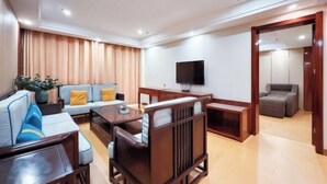 A modern living room with a sofa, armchairs, a coffee table, a TV, and a wooden cabinet. - Pizhou Melvo Hotel (Pizhou)
