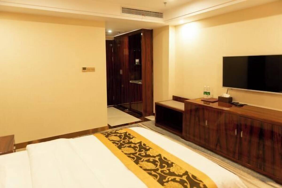 Une chambre d’hôtel avec un lit, une télévision, une armoire en bois et un miroir.