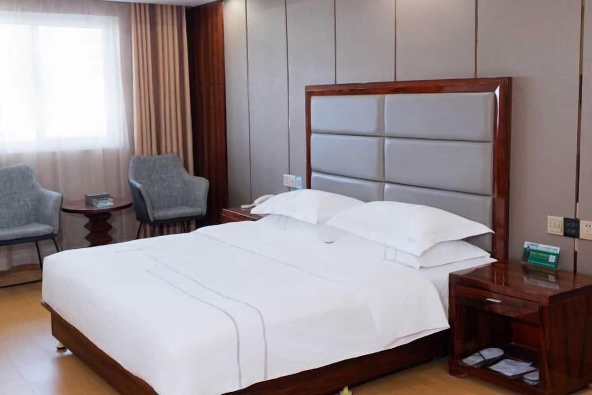 Une chambre d’hôtel avec un grand lit, deux fauteuils, une petite table et une table de chevet.