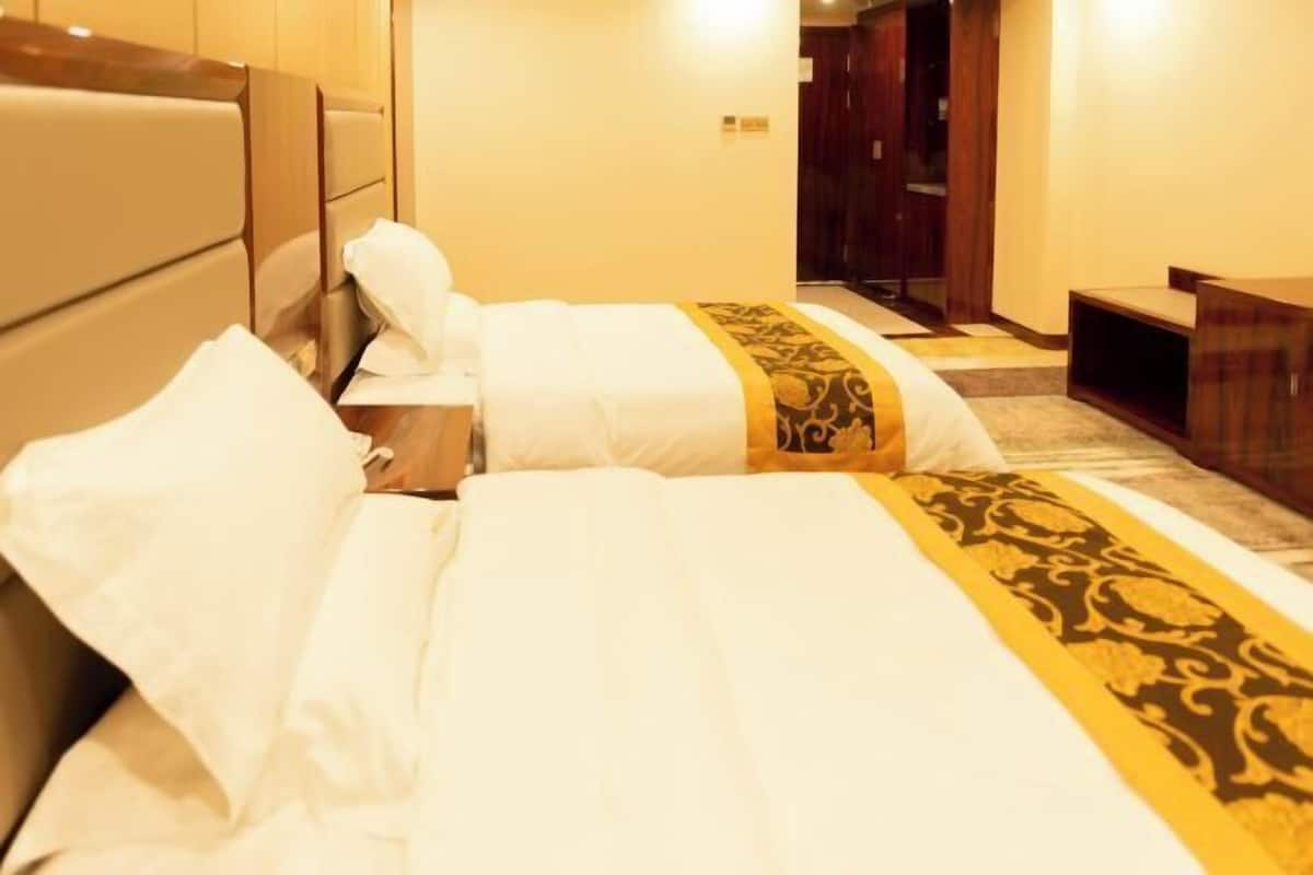 Une chambre d’hôtel avec deux lits, une tête de lit en bois, une table de chevet et un bureau.