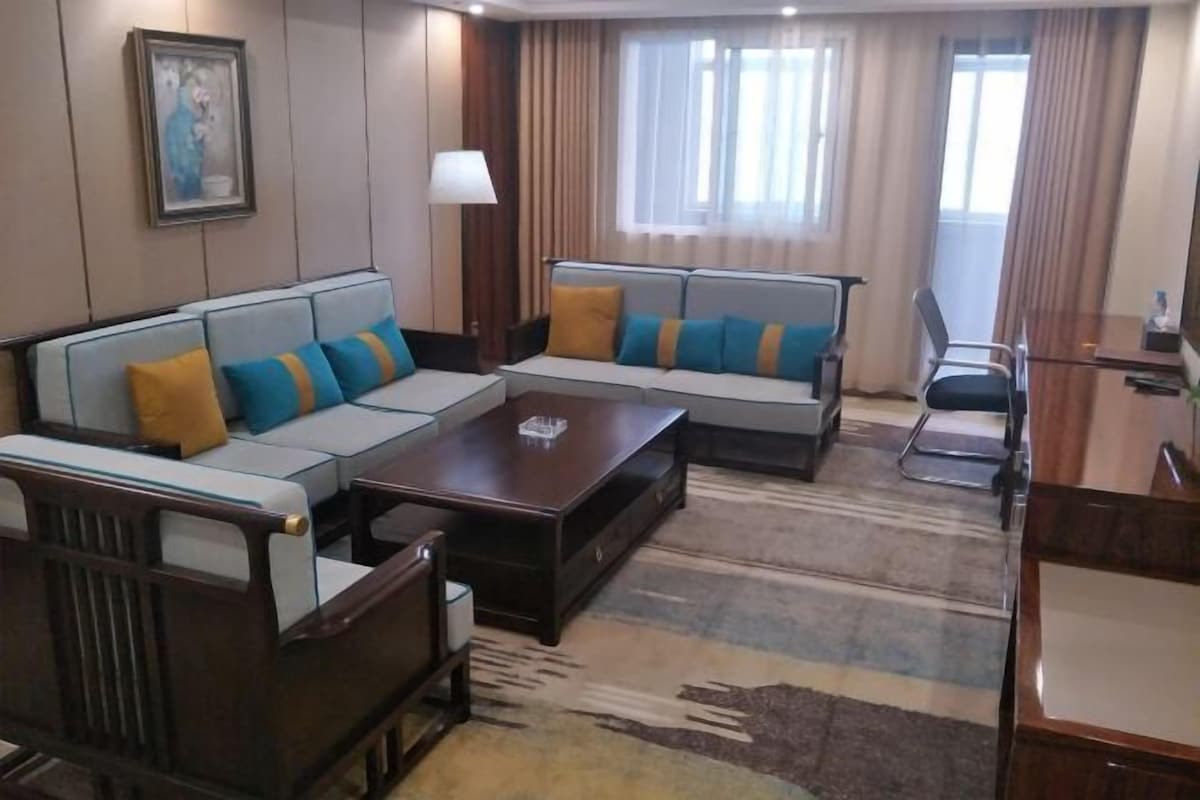 Ein Hotelzimmer mit Ecksofa, einem Holztisch und einem Schreibtisch mit Stuhl.