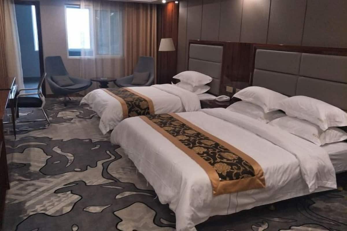 Une chambre d’hôtel avec deux lits, un coin salon avec des fauteuils et une grande fenêtre.