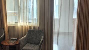 Una habitación con un sillón gris, una mesita redonda y un ventanal con cortinas translúcidas.