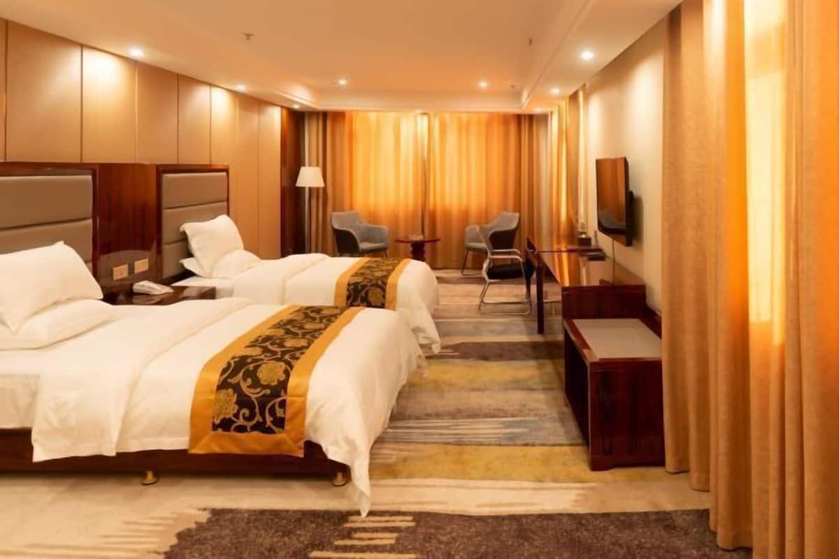Une chambre d’hôtel avec deux lits, un bureau, une chaise, une télévision et une grande fenêtre avec des rideaux.
