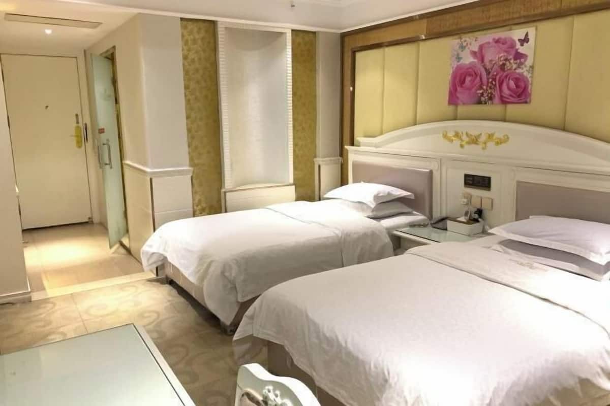 Una habitación de hotel con dos camas, una mesita de noche con lámpara, un reloj en la pared y una puerta.