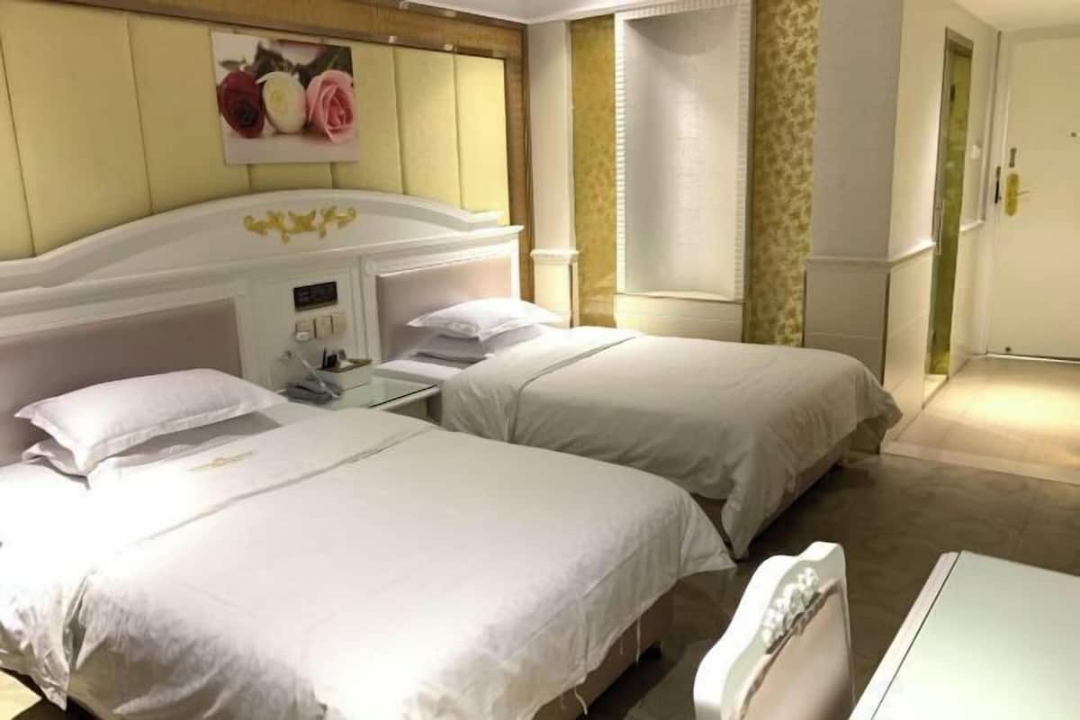Una habitación de hotel con dos camas, una mesita de noche con lámpara y un pequeño escritorio con silla.
