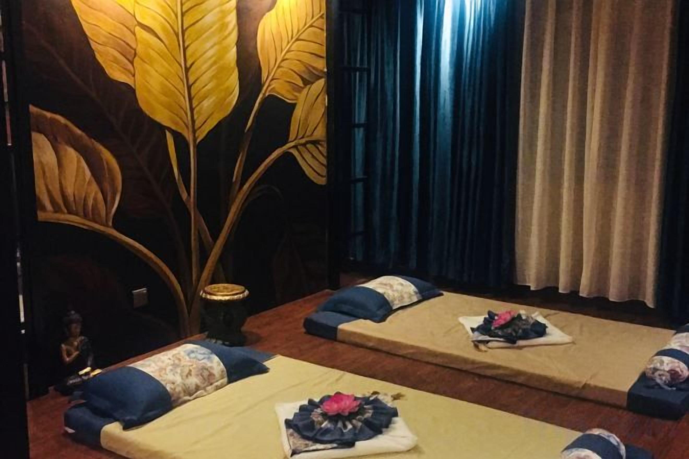 Een kamer met massagetafels, een grote sierplant en gordijnen.