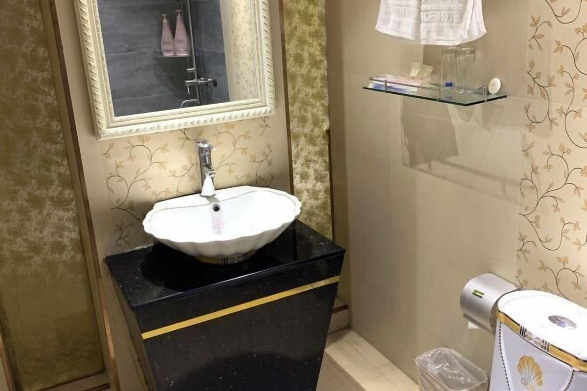 Een badkamer met een wit wastafelmeubel op een zwarte aanrecht, een spiegel erboven en een glazen plank met toiletartikelen.