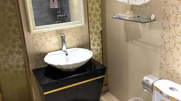 A bathroom with a white sink on a black countertop, a mirror above it, and a glass shelf with toiletries.