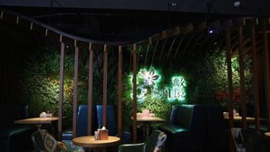 An indoor seating area with round tables and chairs, surrounded by a green wall with plants and a neon sign. - Moon Palace Hotel Huizhou (Huizhou)